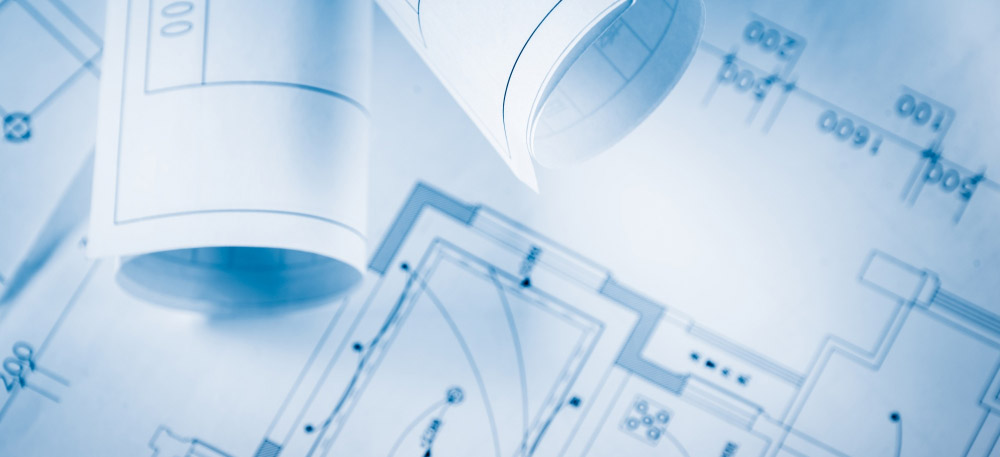 racownik w żółtym kasku ochronnym i rękawicach roboczych sprawdza element stalowy w hali produkcyjnej.